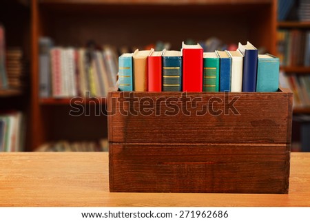 Books in wooden crate on bookshelves background