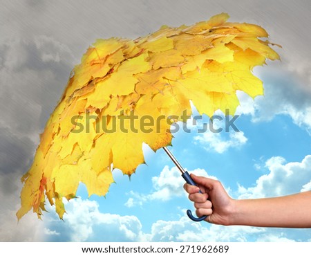 Umbrella  with autumn leaves in hand protecting good weather from dark clouds of rain