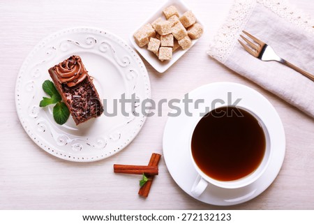 Tasty piece of chocolate cake with mint and cinnamon near cup of tea and lump sugar on wooden table background