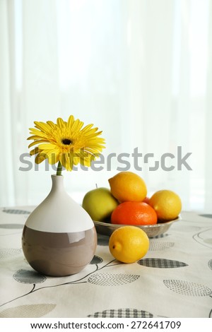 Color gerbera flower in vase and fruits on table on curtains background