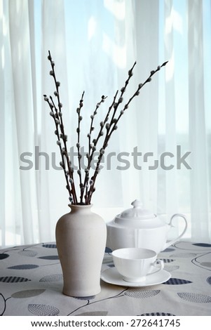 Willow twigs in vase with teapot and cup on table on curtains background
