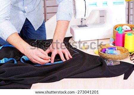 Male dressmaker drawing line on fabric on table close-up