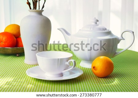 Willow twigs, teapot, cups and citrus on table on curtains background