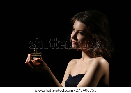 Beautiful woman with perfume bottle on black background