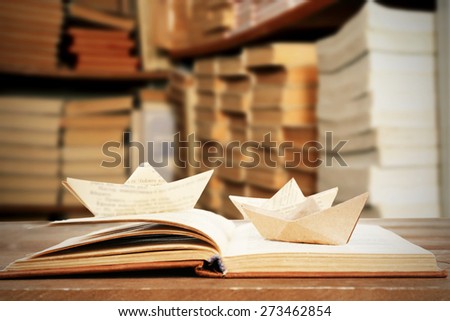 Open book with paper boats on bookshelves background