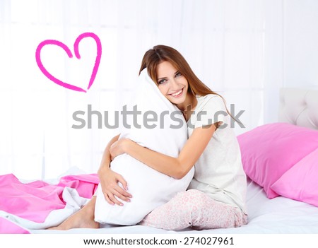 Beautiful young woman dreaming about love and sitting on bed