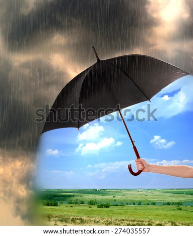 Black umbrella in hand protecting good weather from dark clouds of rain