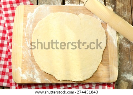 Rolled dough on cutting board with rolling pin on table close up
