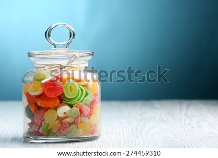 Colorful candies in jar on table on blue background