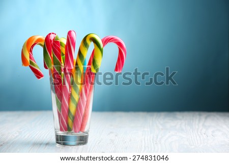 Colorful candy canes in glass on table on blue background