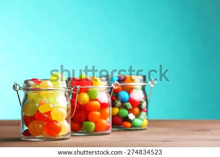 Colorful candies in jars on table on blue background
