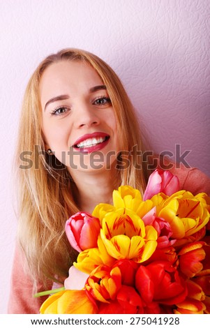 Portrait of young woman with beautiful bouquet of tulips on wallpaper background