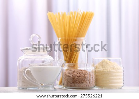 Pasta in glass bottle with cream and different types of flour on wooden table on curtain background