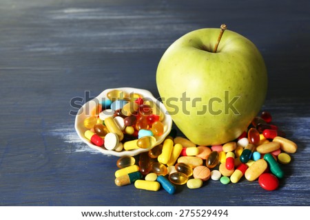 Apple and colorful pills, on color wooden background