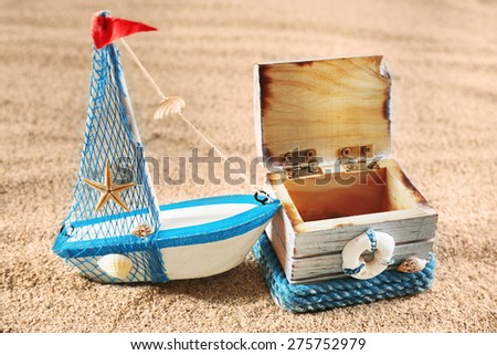 Toy model of ship with wooden box on sea sand background