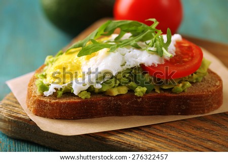 Tasty sandwich with egg, avocado and vegetables on cutting board, on color wooden background