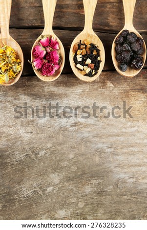 Collection of tea and natural additives in wooden spoons, on old wooden table
