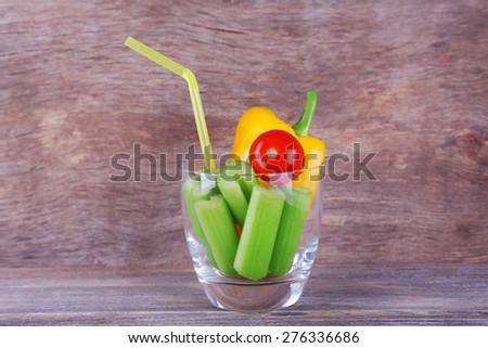 Sticks of celery with sweet pepper and cherry tomato in glass with tube on rustic wooden background