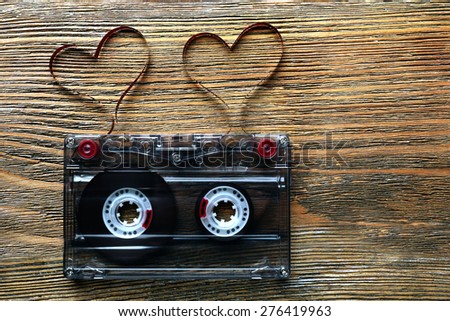 Audio cassette with magnetic tape in shape of hearts on wooden background