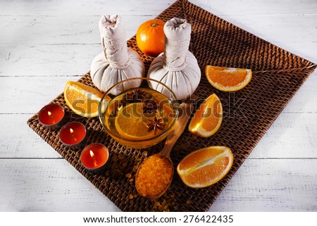 Accessories for massage therapy with candle light, spoon and bowl of essential oil on wicker mat, on color wooden background