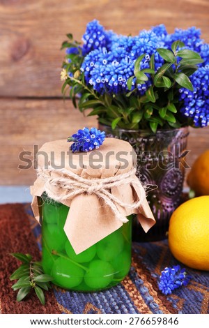 Blue bell flowers with lemon and maraschino cherry in glass jar on wooden background