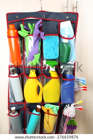 Household chemicals in holder hanging on wooden door background