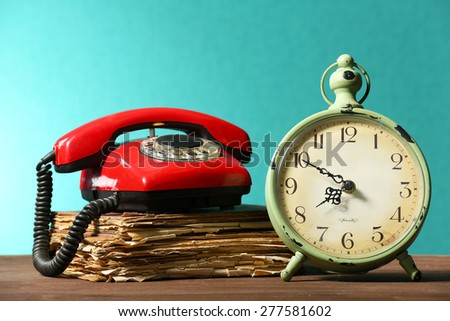 Retro clock with old book and telephone on table on green background