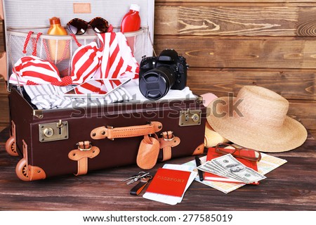 Packed suitcase of vacation items on wooden background
