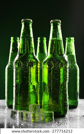 Glass bottles of beer with ice cubes on dark green background