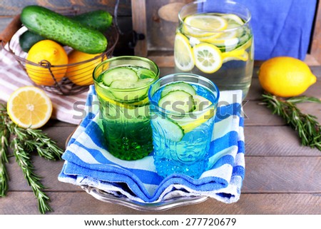 Fresh water with lemon and cucumber in glassware with napkin on wooden background