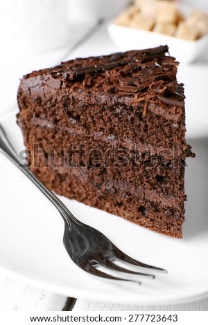 Piece of delicious chocolate cake in plate with fork on color wooden table background