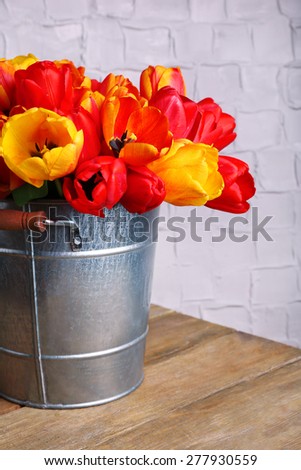 Beautiful bouquet of tulips in metal bucket on wall background