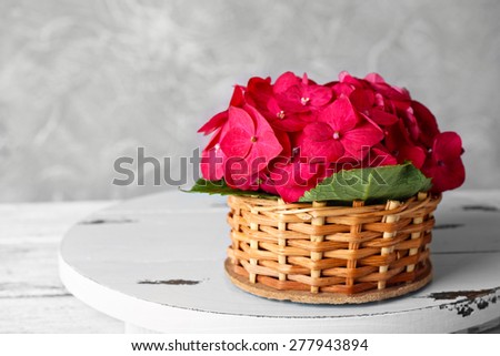 Pink hydrangea in wicket basket on wooden stand on light wallpaper background