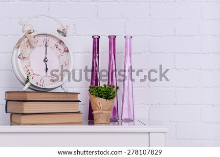 Interior design with alarm clock, plant, decorative vases and stack of books on tabletop on white brick wall background