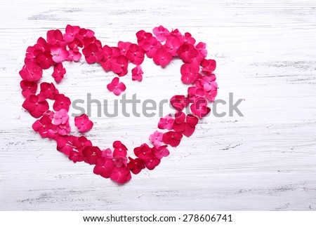 Petals of pink hydrangea in shape of heart on wooden background
