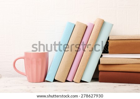 Books and cup on wooden shelf on wallpaper background