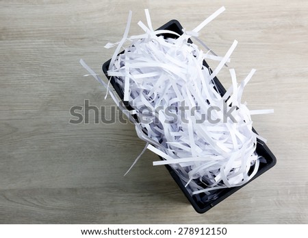 Strips of destroyed paper from shredder in trash can on wooden background