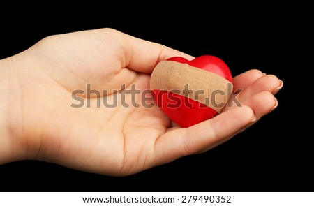 Female hand holding heart with plaster on black