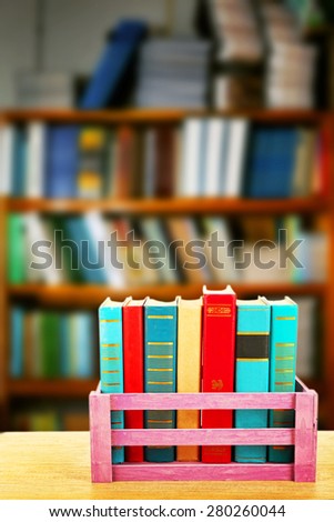 Books in wooden crate on bookshelves background