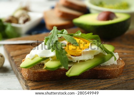 Tasty sandwich with egg, avocado and arugula on wooden background