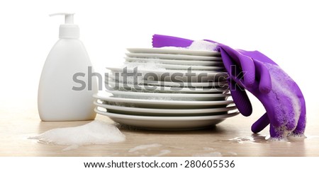 Plates in foam with gloves and cleanser on table isolated on white