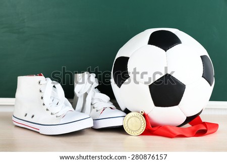 Sport shoes, soccer ball and golden medal on blackboard background