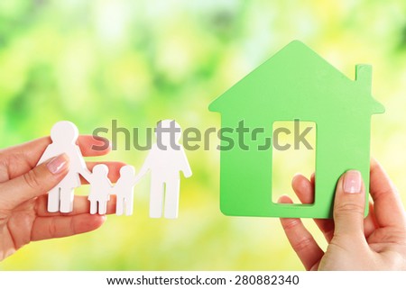 Female hands holding model of house and paper family on bright background