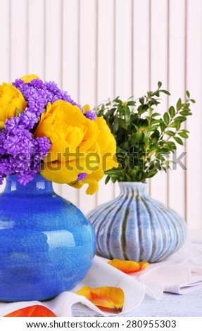 Composition with fresh spring flowers in ceramics vases on wooden background