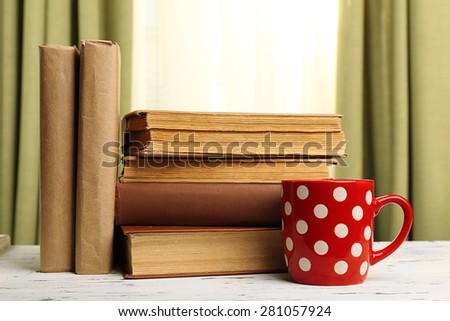 Books and cup on wooden table, on curtains background