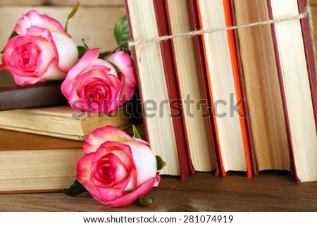 Tied books with pink roses on wooden table, closeup