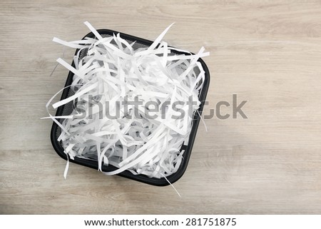 Strips of destroyed paper from shredder in trash can on wooden background