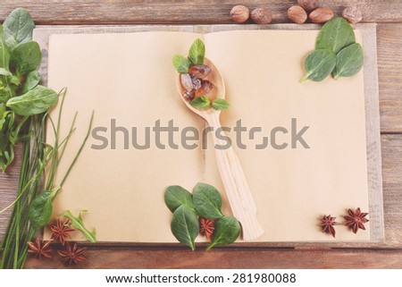 Open recipe book with spoon and herbs on wooden background