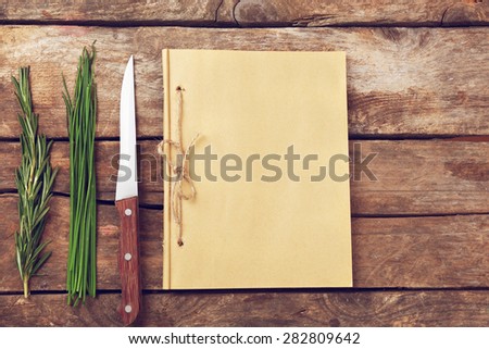 Recipe book page with knife and herbs on wooden background