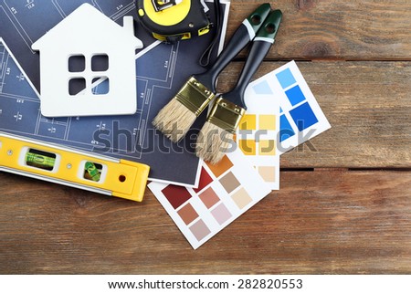 Color samples, decorative house, gloves and paintbrushes on wooden table background